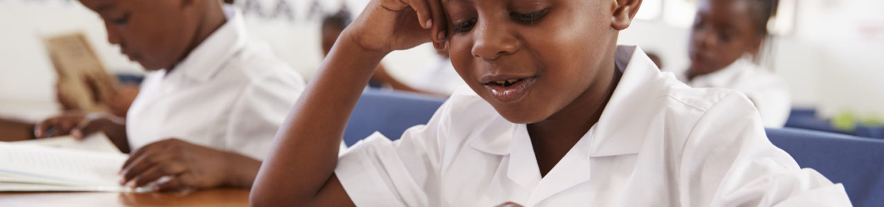 Elementary school boy reading a book at his desk in class